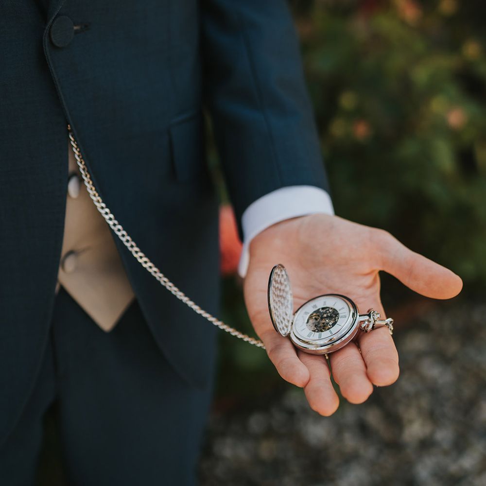 Groom in navy suit holding silver pocket watch groom accessory 