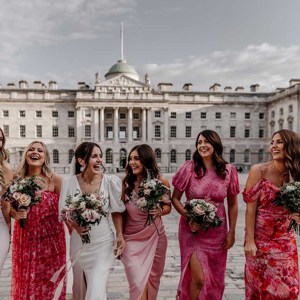 Bride in puff sleeve front leg slit wedding dress walking with bridesmaids in mismatched summery pink bridesmaid dresses 