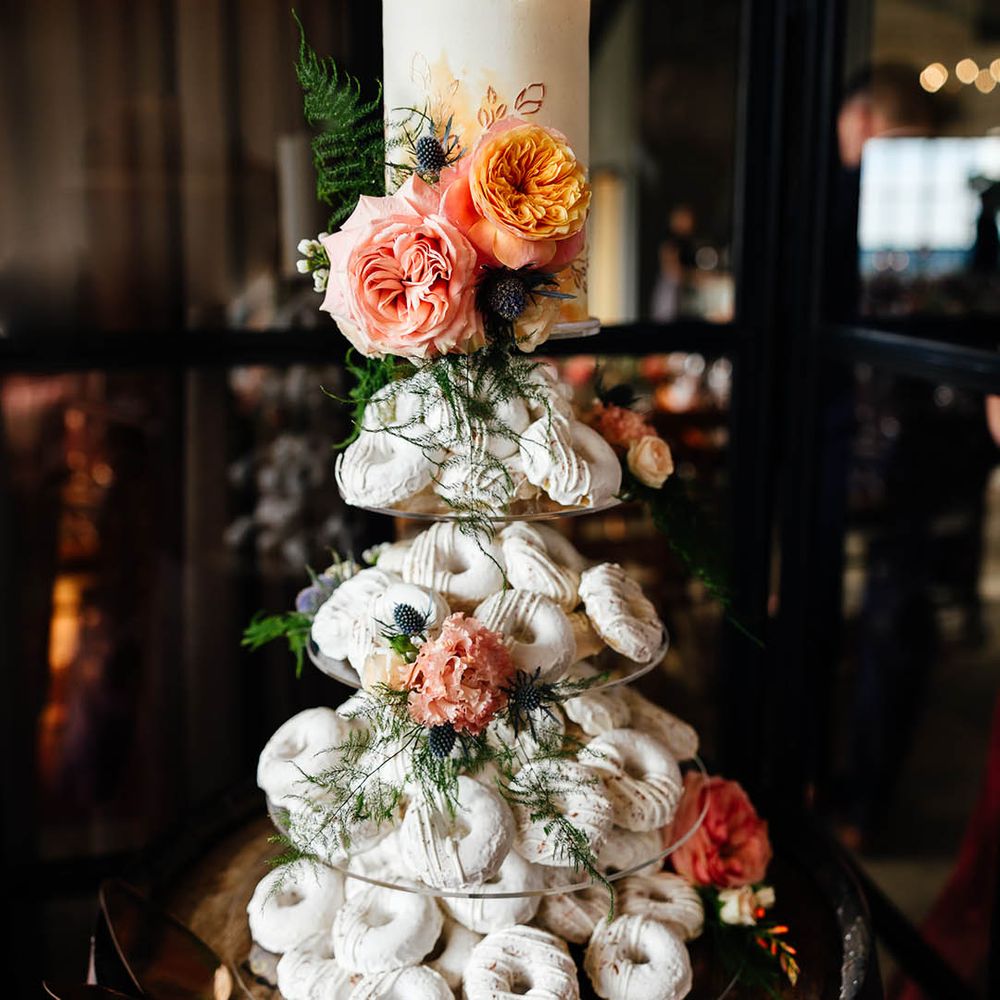 Doughnut tower made of white doughnuts with white iced wedding cake layer decorated with pink flowers 