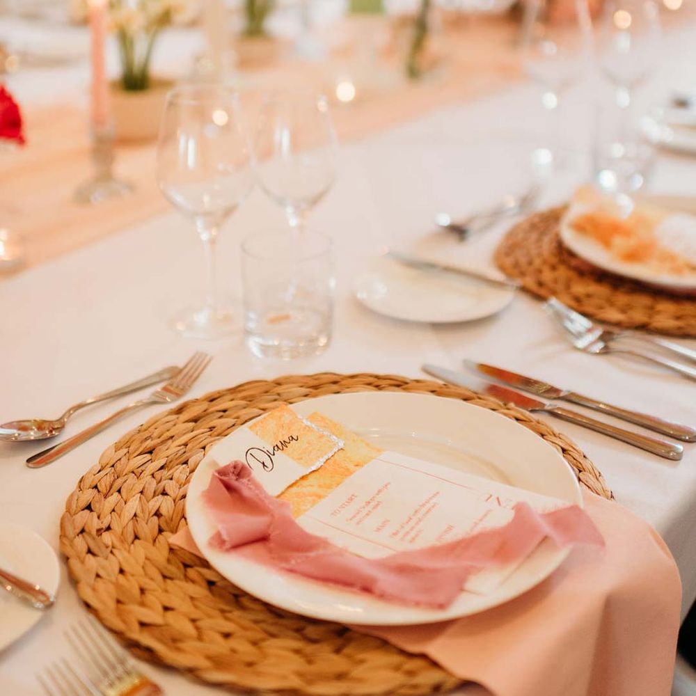 Wedding tablescape with white wedding tablecloth, burlap place mats, tapered candles, pink and orange wedding stationery, and floral wedding table centrepieces