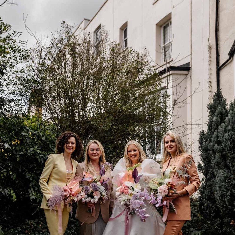 Bride in dramatic satin wedding dress with large puff sleeves standing with bridesmaids in mismatched pastel satin bridesmaid suits - hen party ideas