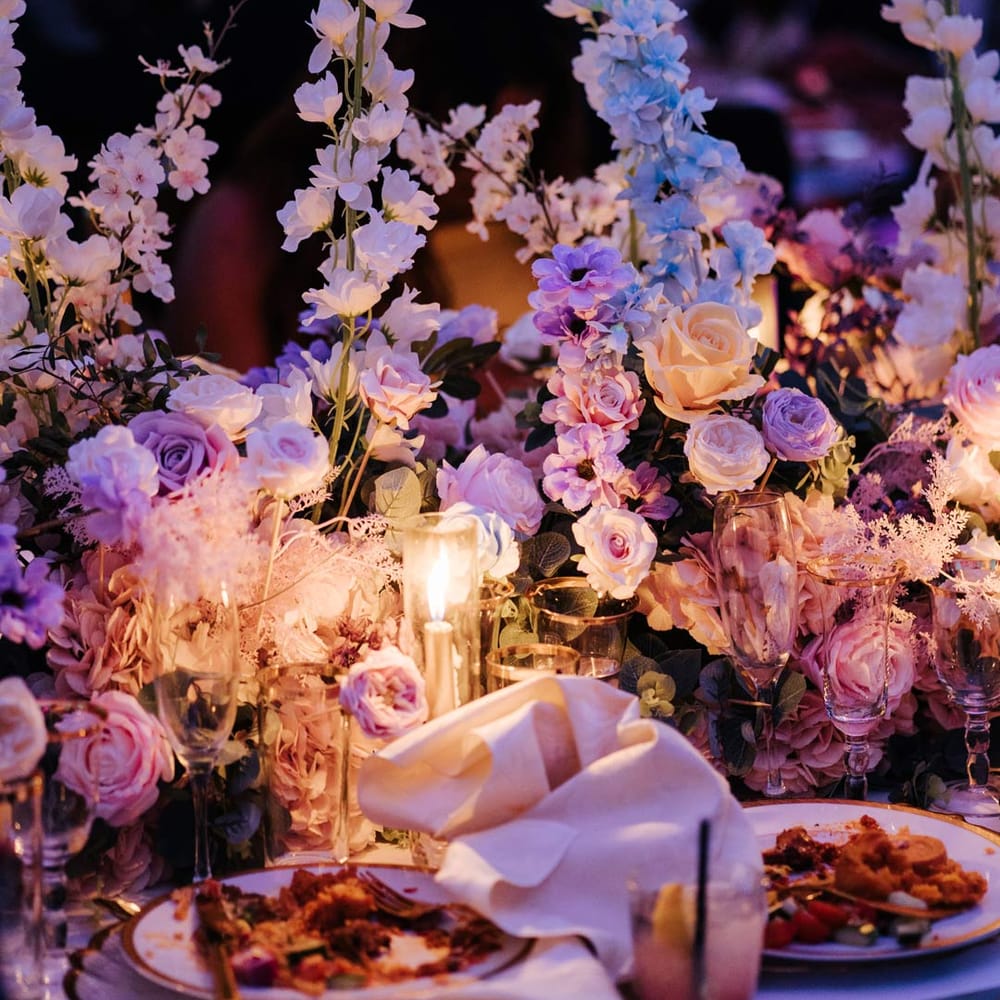 Botanical wedding tablescape at Syon Park vow renewal with large pastel flower centrepieces, gold tapered candles, gold rimmed tableware and suspended pastel foliage decor 