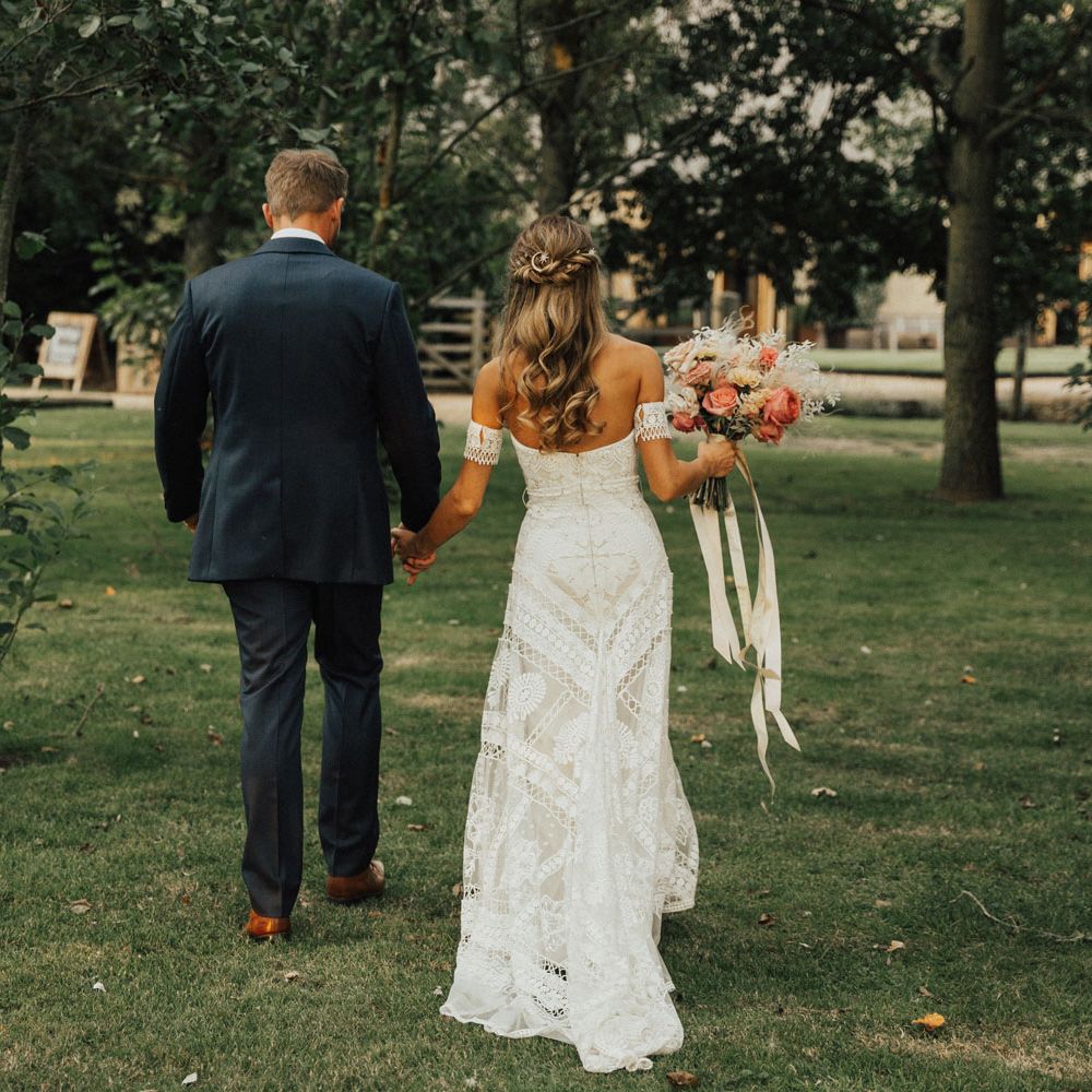 Bride in boho Rue De Seine wedding dress and Groom in bespoke navy suit walk off together holding hands