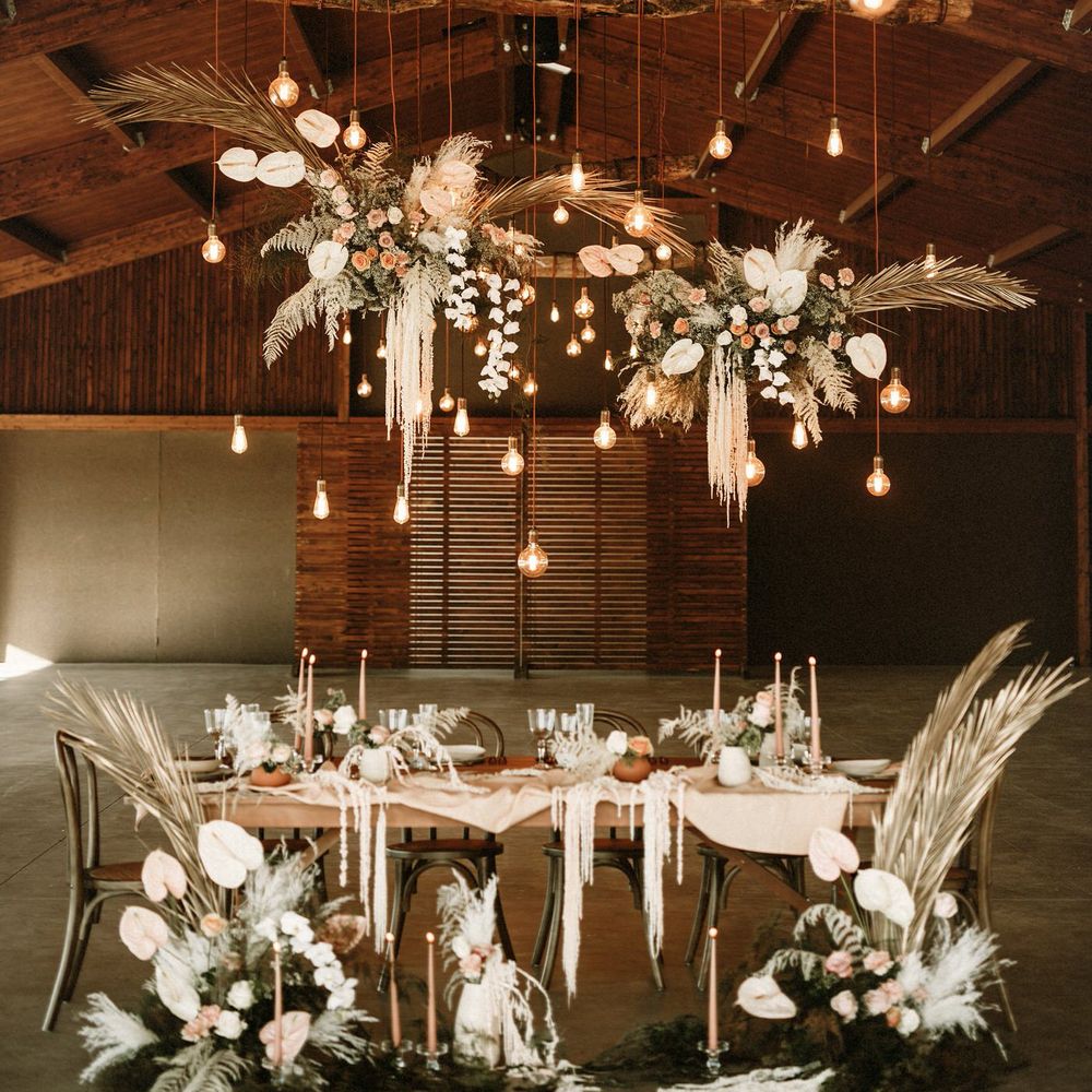 Barn wedding venue decorated with an intimate tablescape full of boho wedding flowers, taper candles, natural linens and festoon light installation 