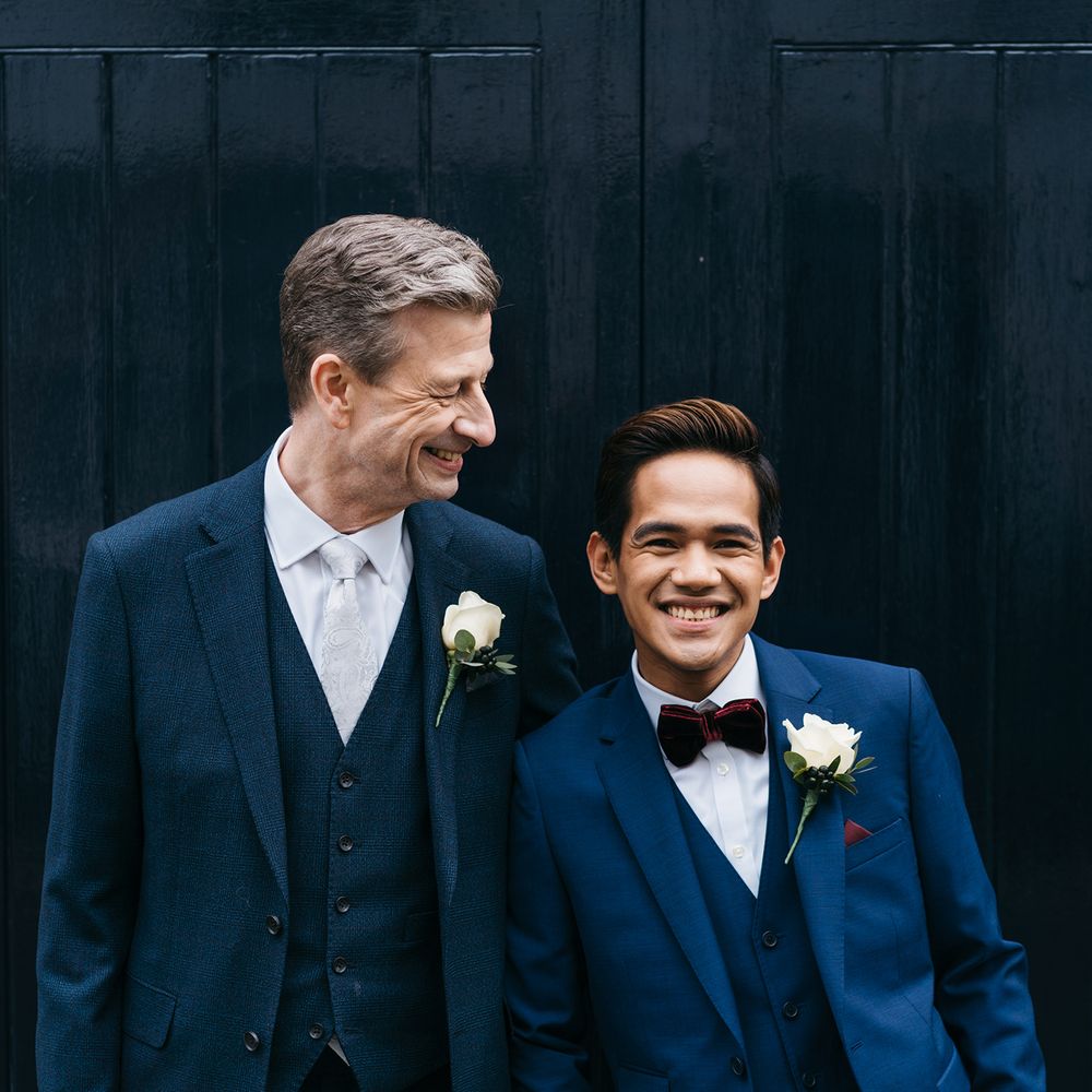 Grooms laugh and stand together wearing blue suits
