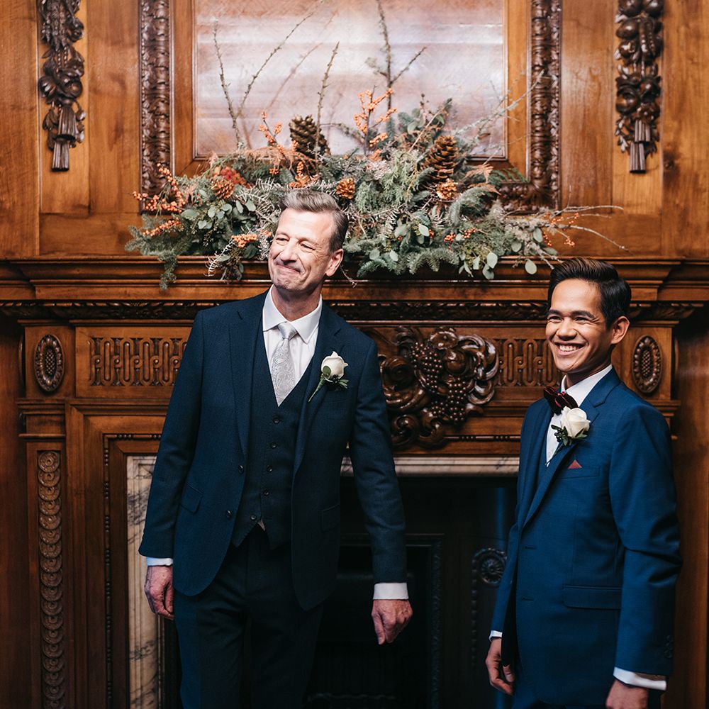 Grooms stand together in front of wooden fireplace at the Old Marylebone Town Hall