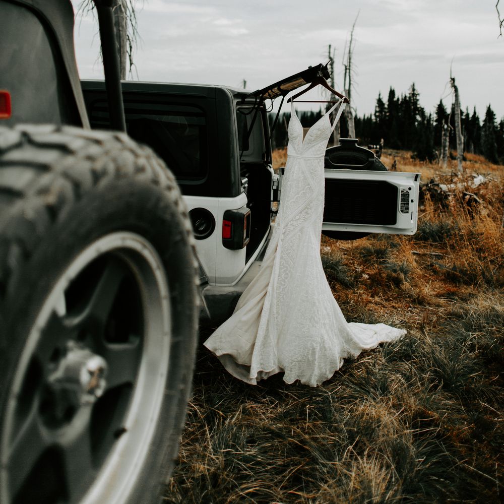 Bridal gown hangs on white Jeep before wedding ceremony