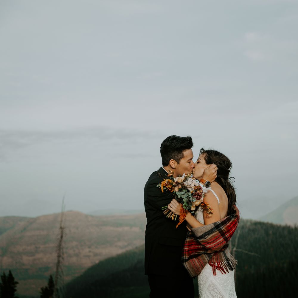 Bride & groom kiss on mountain top whilst bride holds Autumnal bouquet