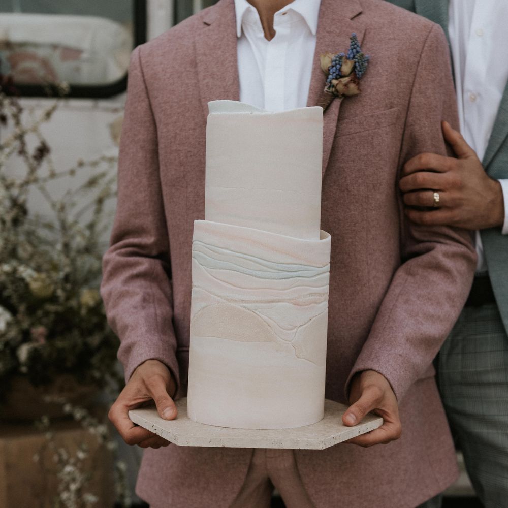 Grooms wears pastel suits whilst holding modern wedding cake with pastel colouring