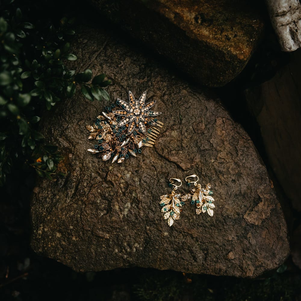 Bejewelled hair comb and leaf earrings laid on rock outside at farm wedding