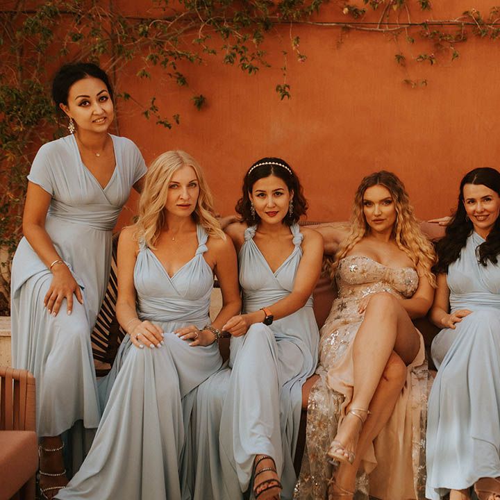 Bride sits with her bridesmaids who wear dusty blue gowns and bride wears dress with detachable skirt