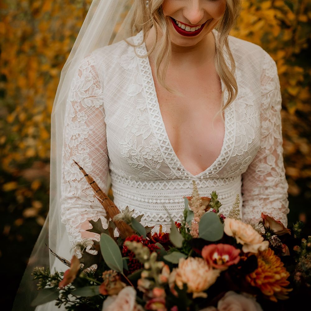 Beautiful bride in a Juliet cap veil with blush cheeks and red lipstick holding her autumnal bouquet 