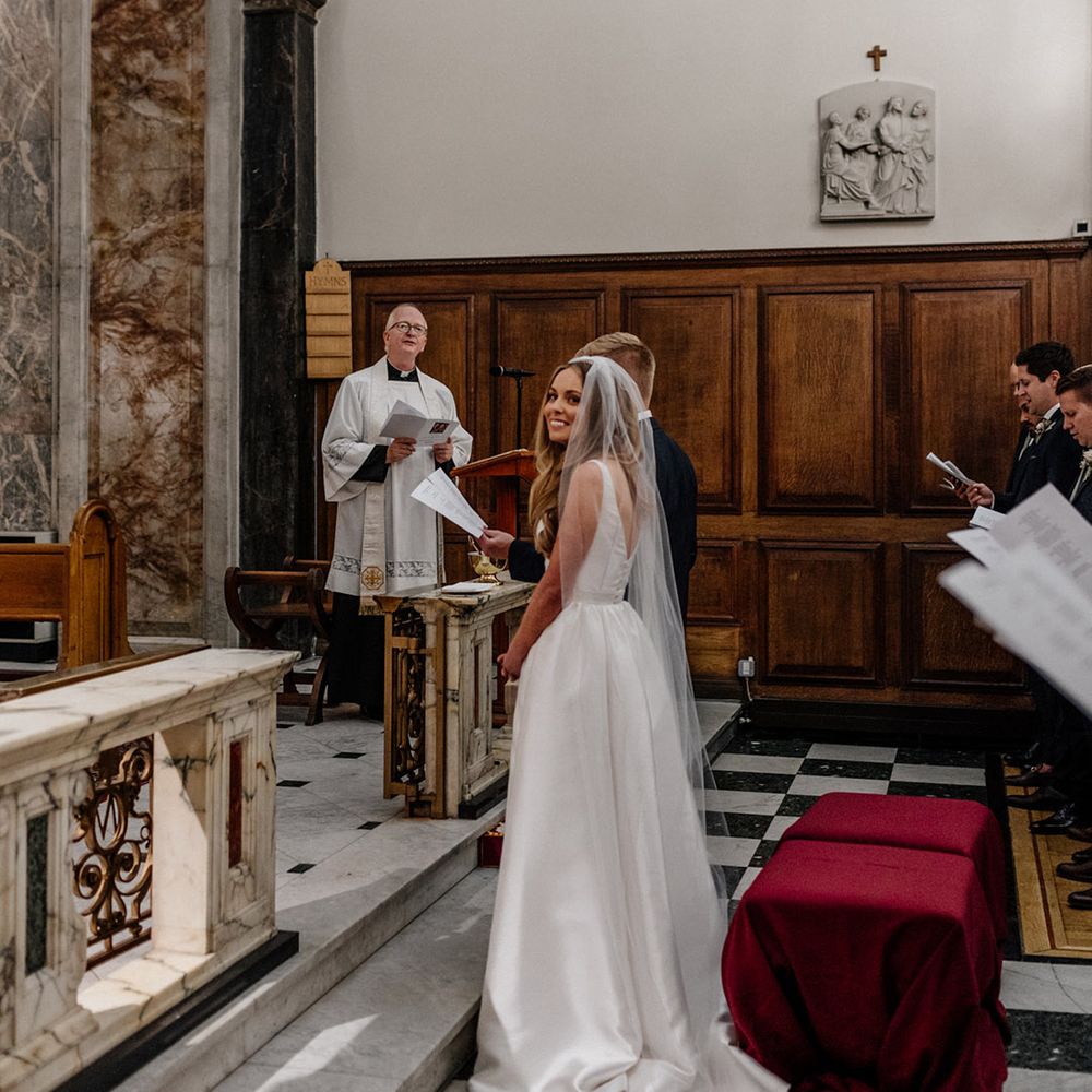 Bride in a Karen Willis Holmes wedding dress with long cathedral length veil standing at the altar 