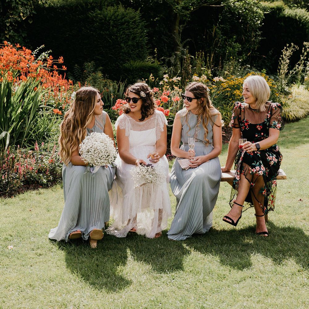 Bride in sunglasses sits with bridesmaids in green pleated dresses and wedding guest