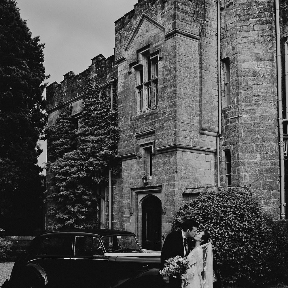 Bride and groom kiss in front of their Bentley wedding car transportation in front of Wadhurst Castle 