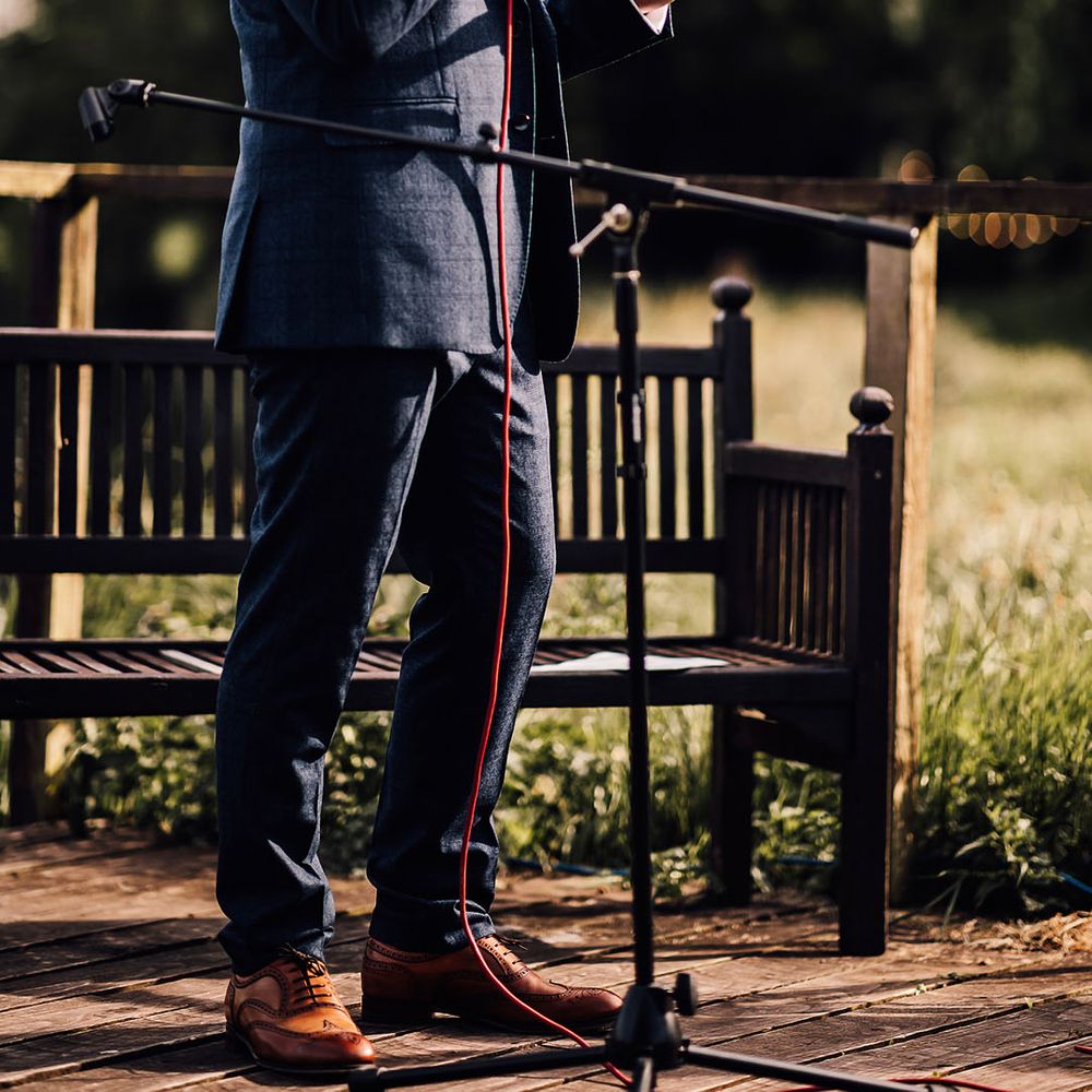 Groom in blue suit and sunglasses reads out his wedding speech 