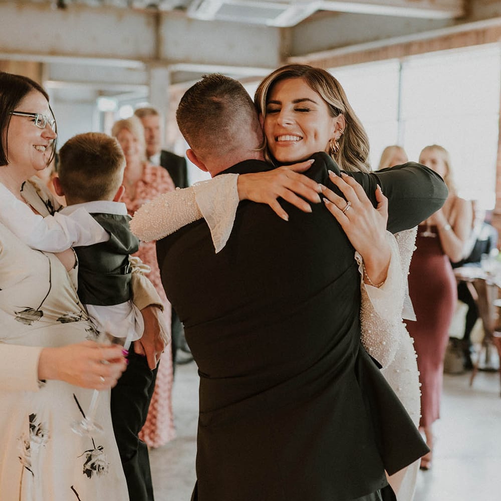 Bride hugs a wedding guest with almond French tip nails with pearls and pearl embellished outfit 