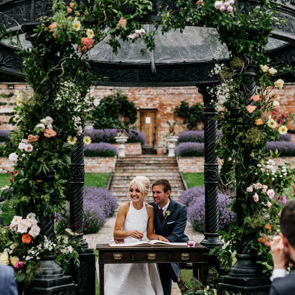 Bride in halterneck wedding dress and colourful bouquet and groom signing the register
