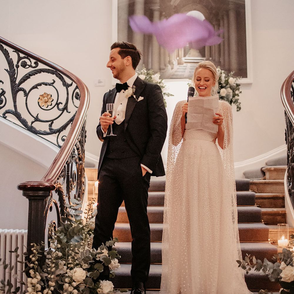 Bride reads out a speech as she stands with the groom in black tie 
