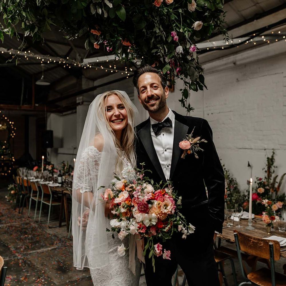 Bride in boho two piece lace bridal outfit with large colourful mixed bouquet and groom in black tux with velvet look bow tie