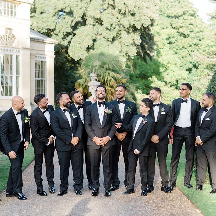 Groom stands with his groomsmen in black tie complete with floral buttonholes and pocket squares 