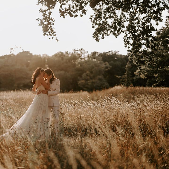 The brides share a kiss in a field during golden hour 