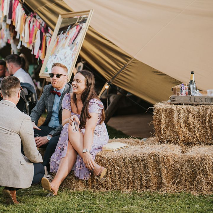 Wedding guests sit on hay bales outdoors 