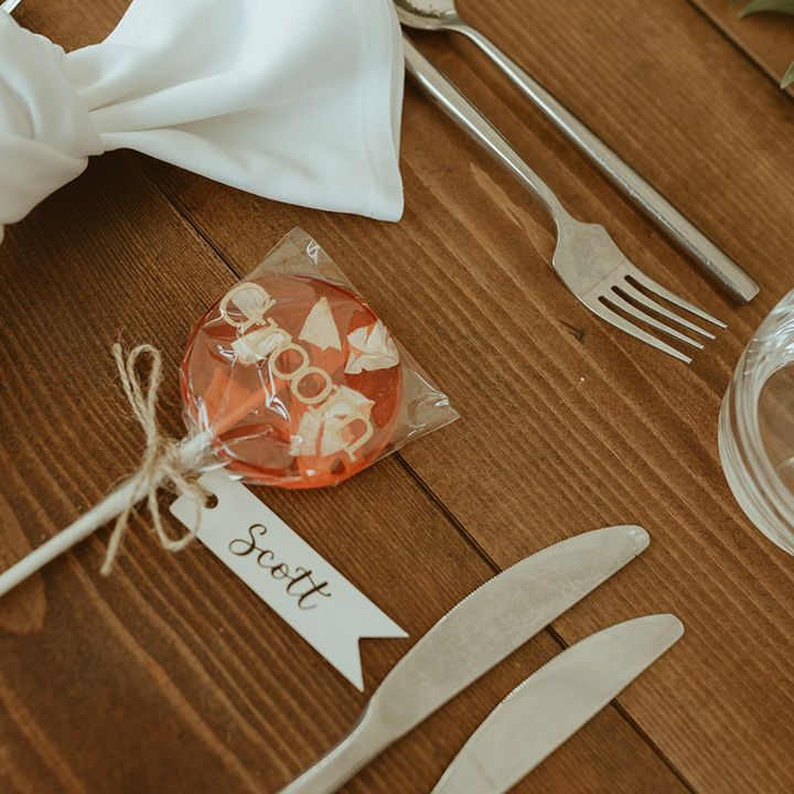 Red lolly wedding favours personalised with names next to white napkins and silver cutlery 