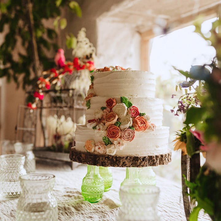 Short three tier white iced wedding cake with iced flowers resting on a tree trunk slice cake stand for the rustic wedding 
