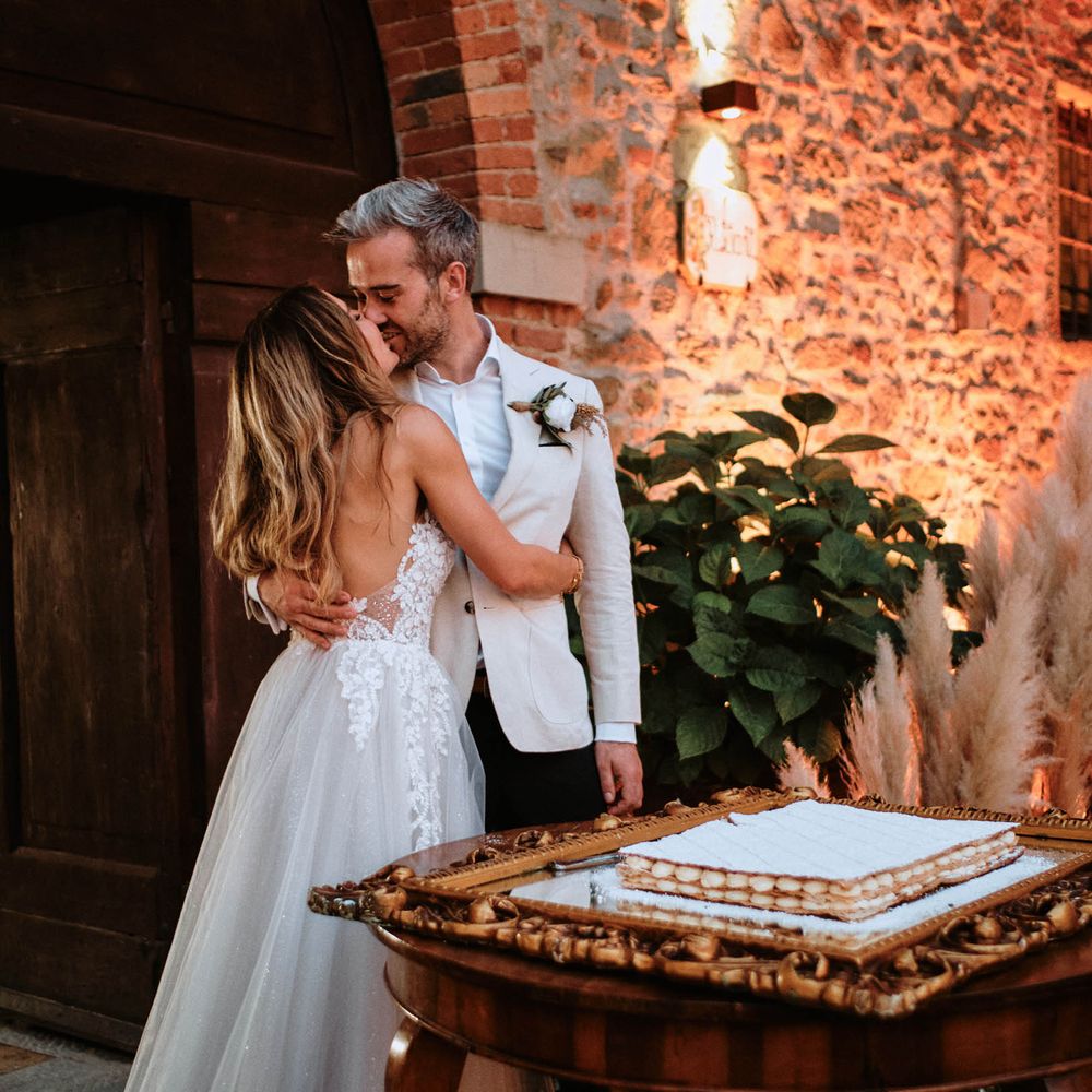 Bride and groom share a kiss next to wedding cake at destination wedding in Tuscany