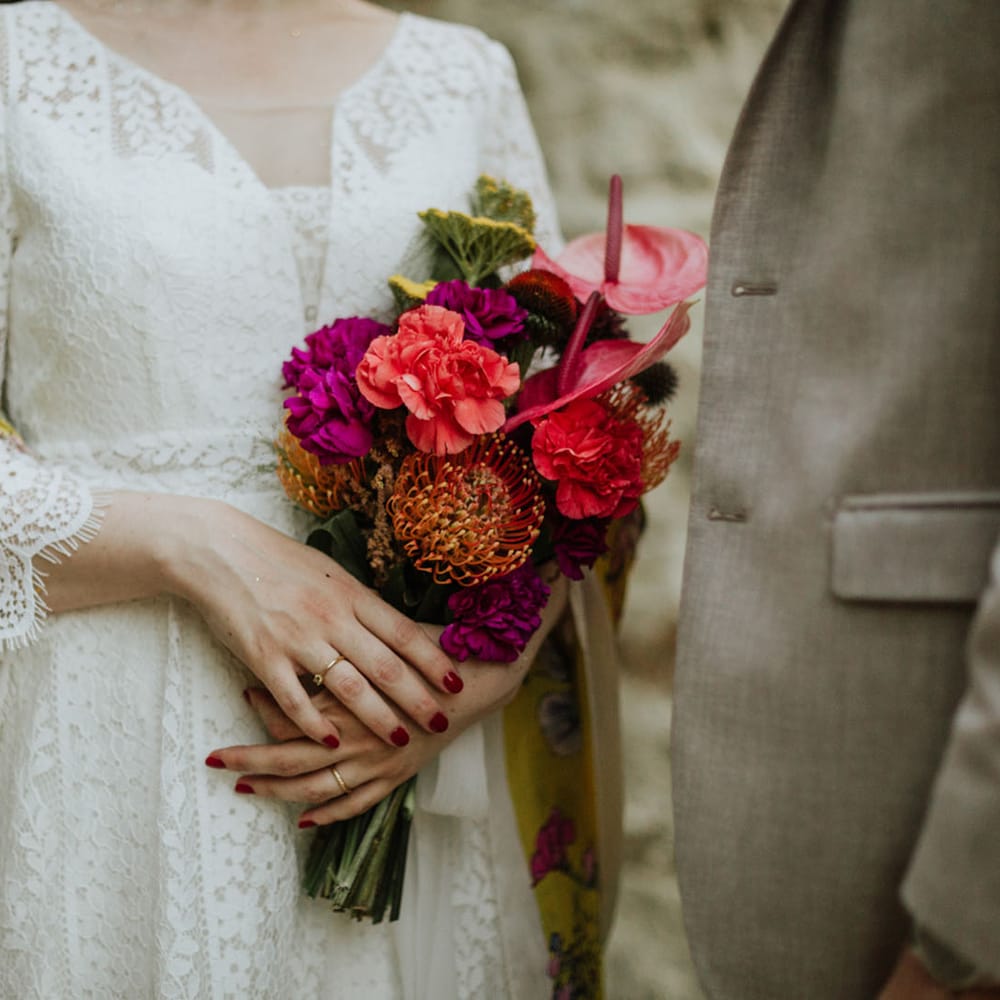 Bridal bouquet consisting of magenta peonies, coral carnations, pink anthuriums, and pincushion flowers