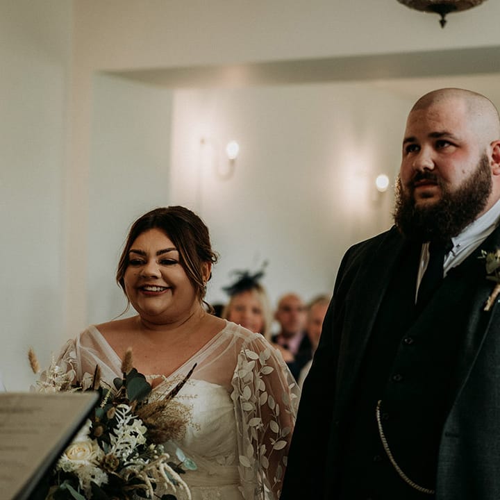 Groom in green tweed wedding suit with the bride in a lace long sleeve wedding dress at modern wedding 