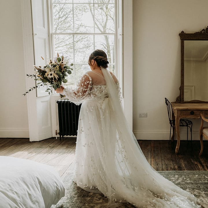 Bride in lace wedding dress with train preparing for first look with father of the bride 