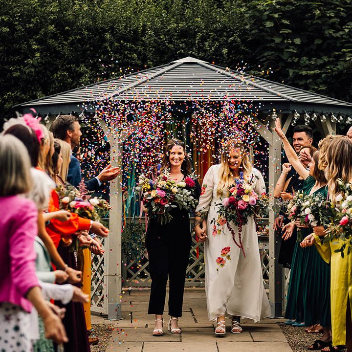 Rainbow colourful confetti moment for two brides as they exit from their same sex wedding ceremony 