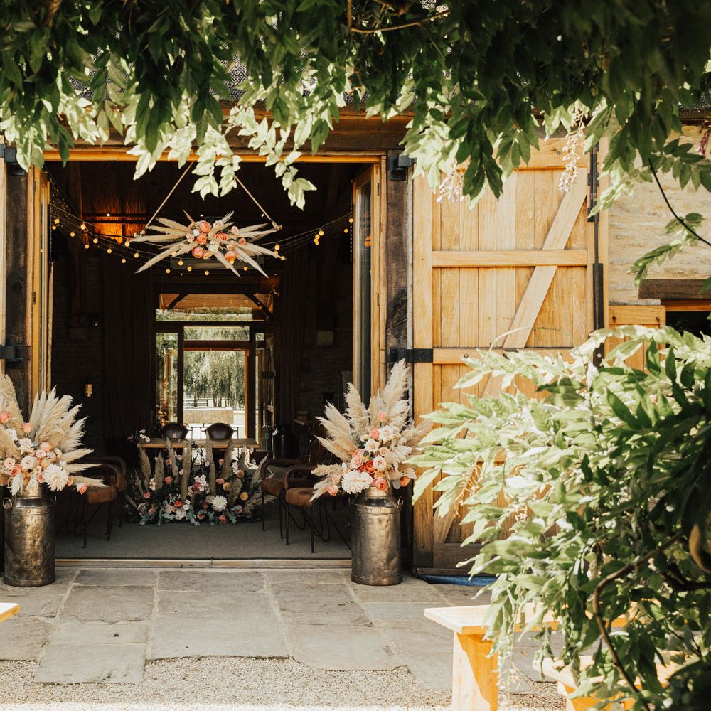 Tythe Barn Wedding ceremony venue with pampas grass cloud, pampas grass and rose floral arrangements and wooden benches