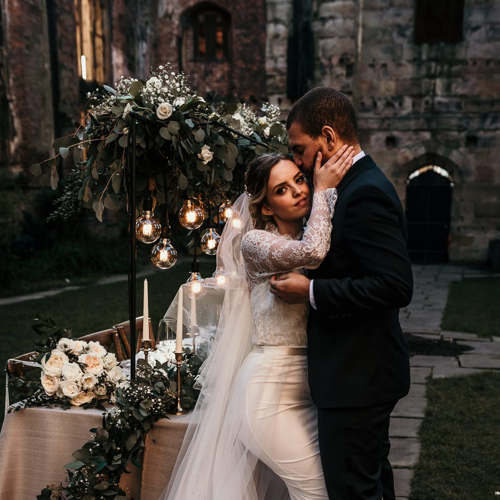 Intimate bride and groom portrait next to their intimate wedding reception table with festoon lights and foliage decor 
