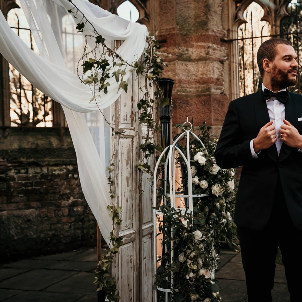 Groom in a black tuxedo standing at the altar of St Lukes' bombed out church in Liverpool 