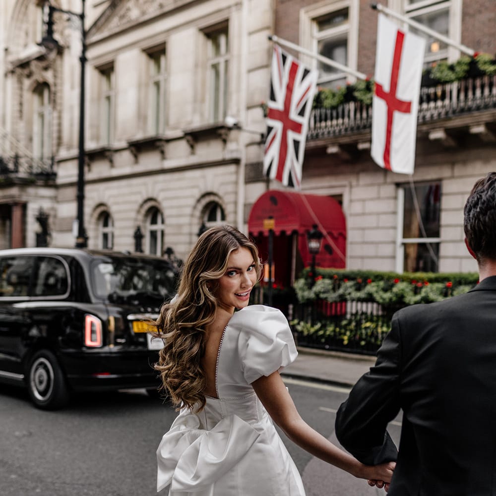 City bride in a short wedding dress with low back and bow detail with long curly hair and pink eyeshadow 