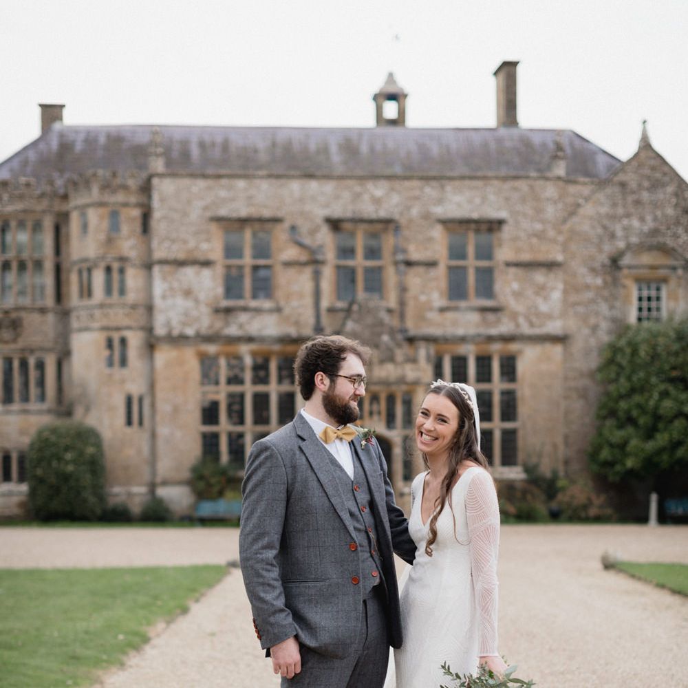 Portrait of the bride in an embellished Eliza Jane Howell wedding dress and the groom in a grey suit standing outside their Brympton House wedding venue 