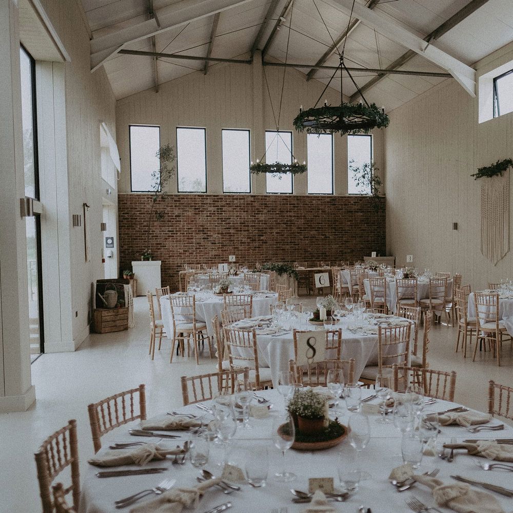 Round tables with white tablecloth and bamboo chairs in barn at East Afton Farmhouse for wedding breakfast with macrame wedding decor 