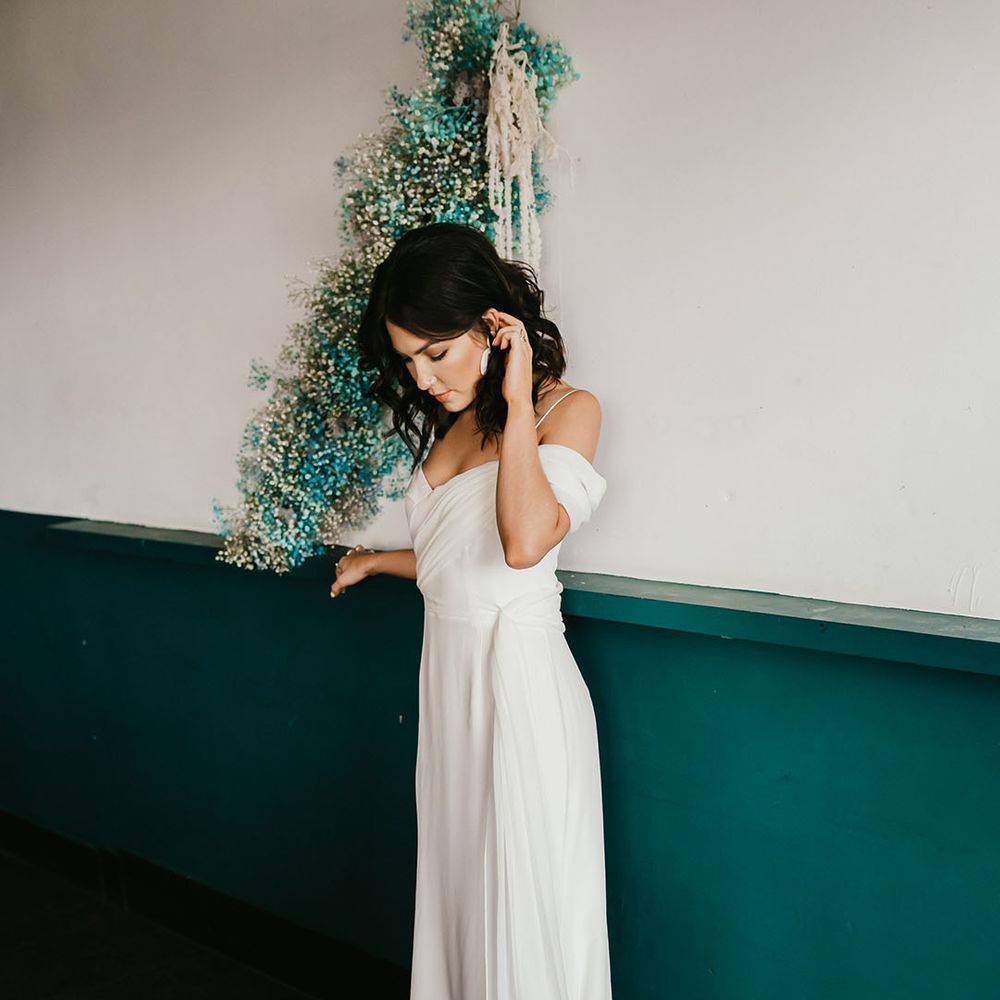Bride in a cold shoulder wedding dress standing next to a white a teal gypsophila flower cloud 