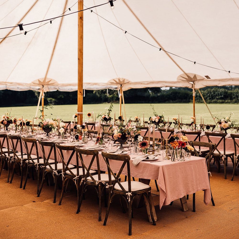 Two long wooden tables with dusky pink tablecloths, candles and assorted florals for marquee garden wedding reception in Cornwall