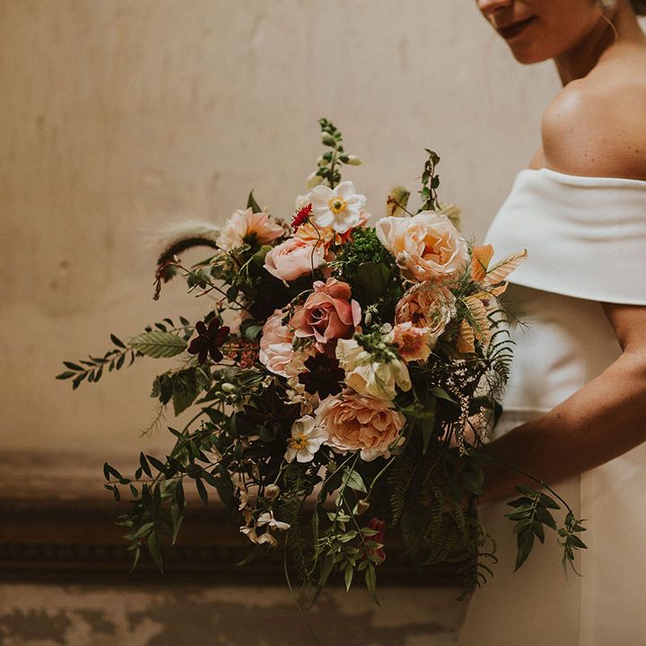 Bride wears off the shoulder wedding gown whilst holding peach and pale pink floral bouquet
