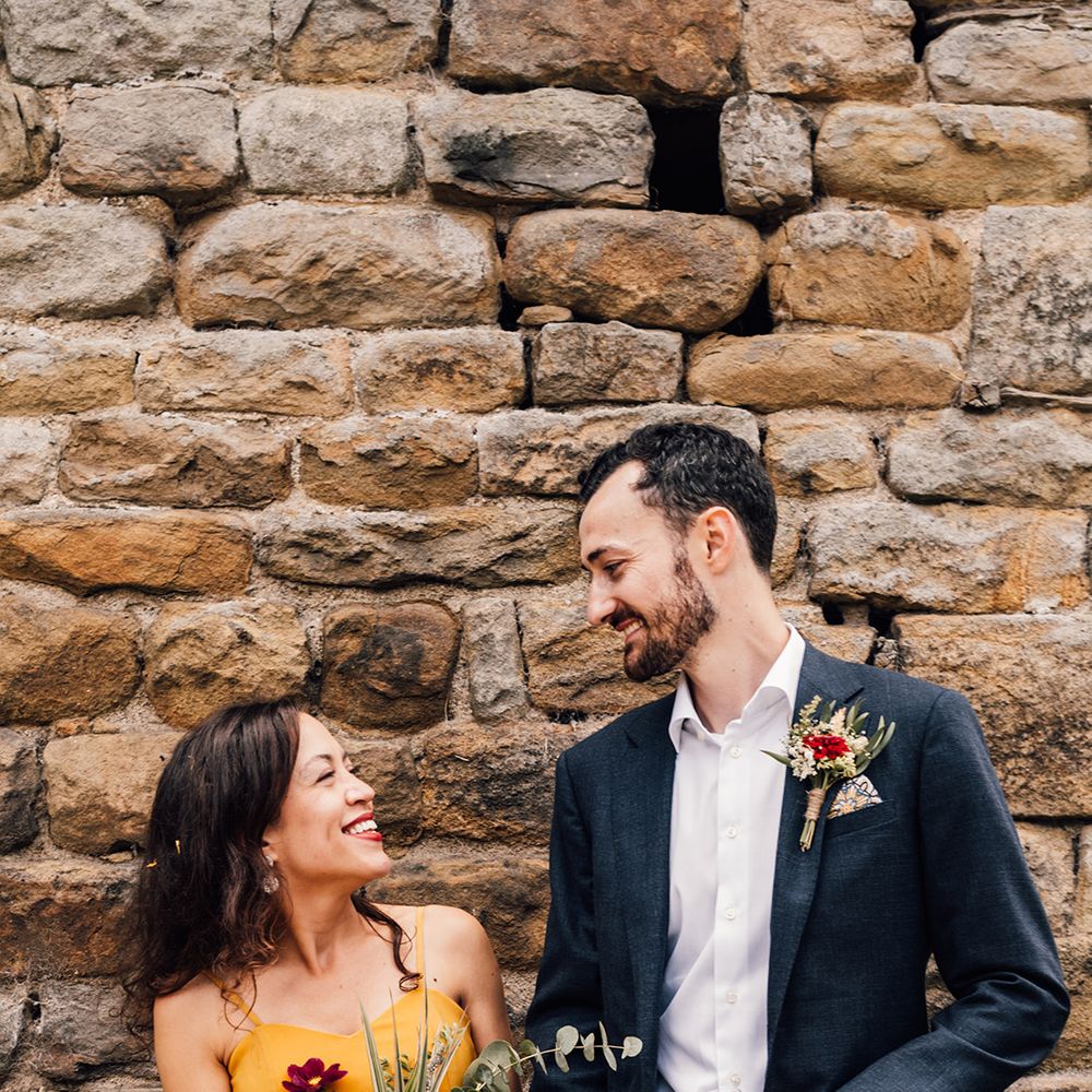 Bride & groom laugh in front of brick wall on their wedding day
