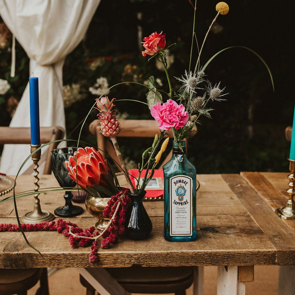 Gin bottles and vessels filled with colourful flower stems wedding table decor 