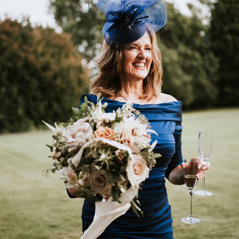Mother of the bride in a navy blue strapless dress and fascinator holding the romantic wedding bouquet tied with ribbon 