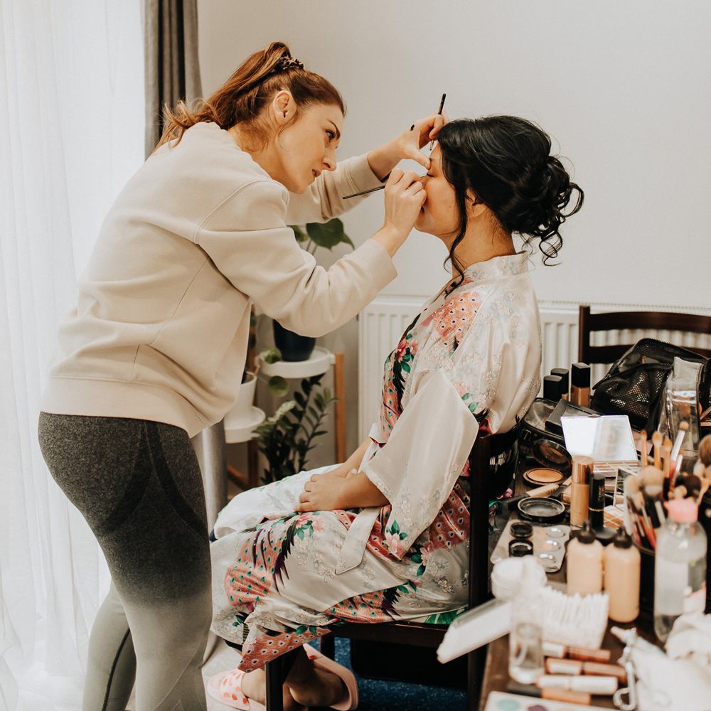 Bride in patterned silk kimono dressing gown sits having her makeup done before wedding