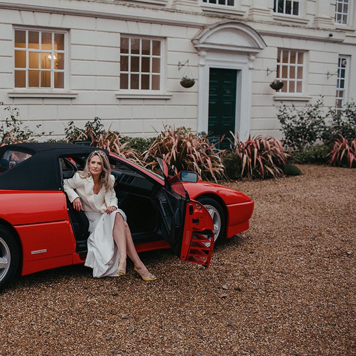 Bride sits in red Ferrari on her wedding day in front of Gosfield Hall