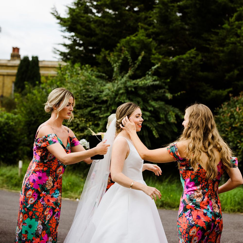 Bridesmaids in bright green, red, pink, blue floral dresses help bride with the final touches 