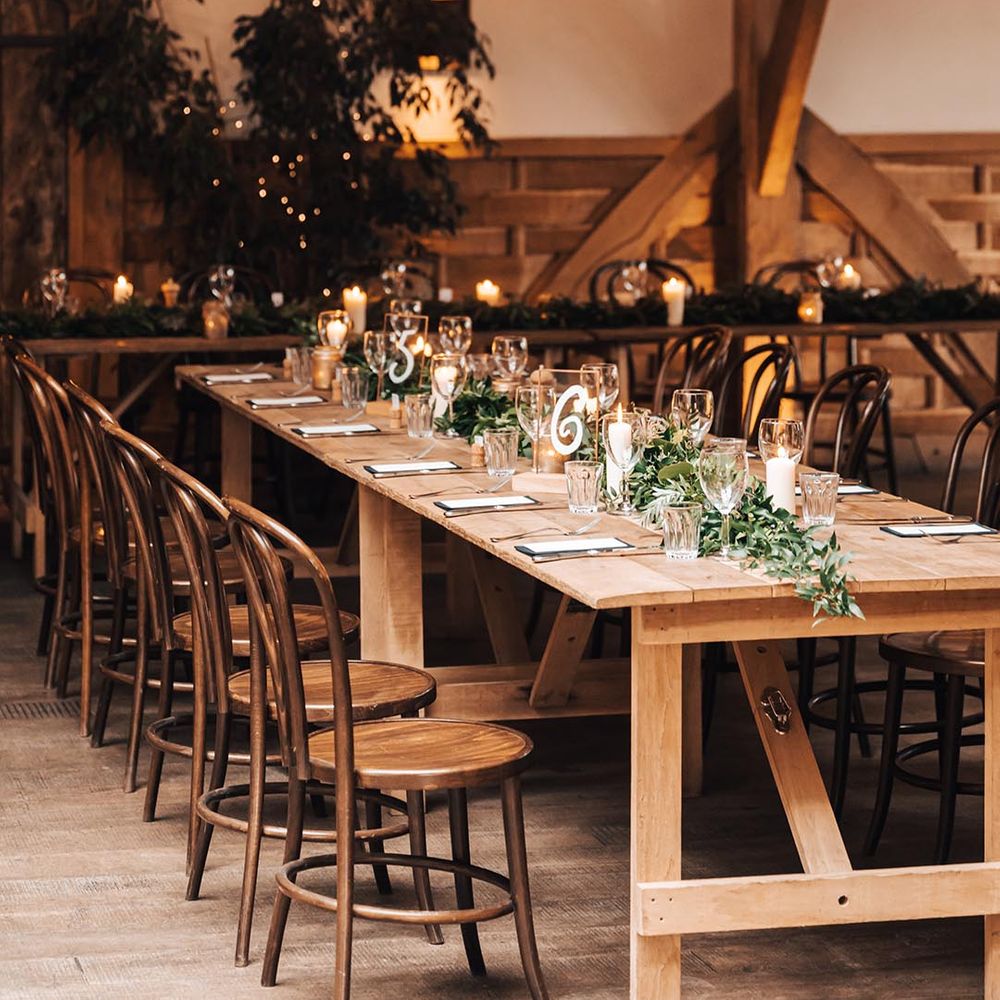 Cripps Barn wedding reception with wooden table decorated with a foliage runner and pillar candles 